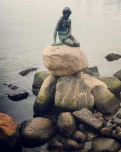 Mermaid statue on coastal boulders.