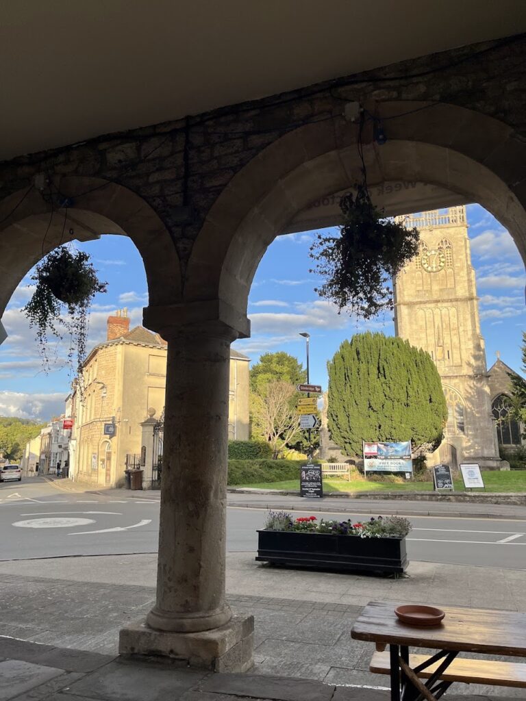 View through dual arches to a British stone church bordered by trees, blue sky in the background.